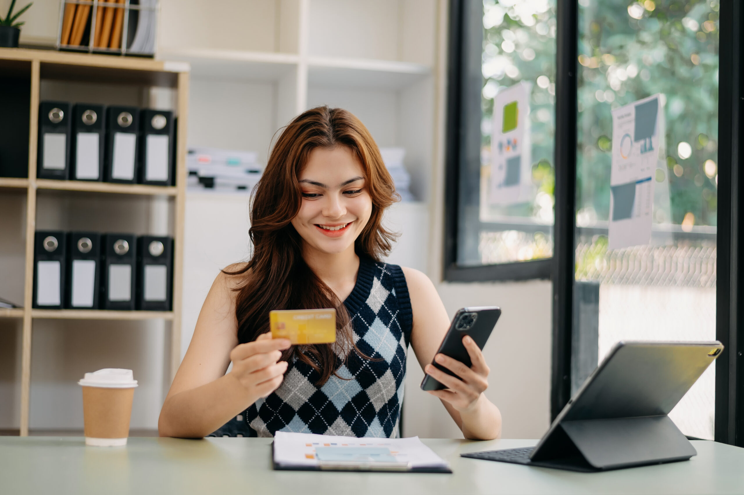 businesswoman hand using smart phone, tablet payments and holding credit card online shopping, omni channel, digital tablet docking keyboard computer at office in sun light